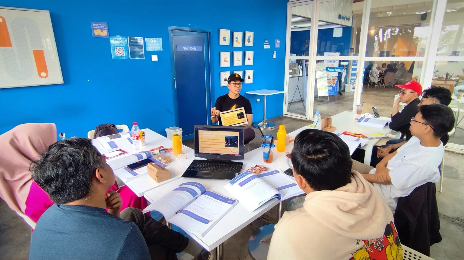 My First Bitcoin instructor presenting a slide to students seated around cafe tables
