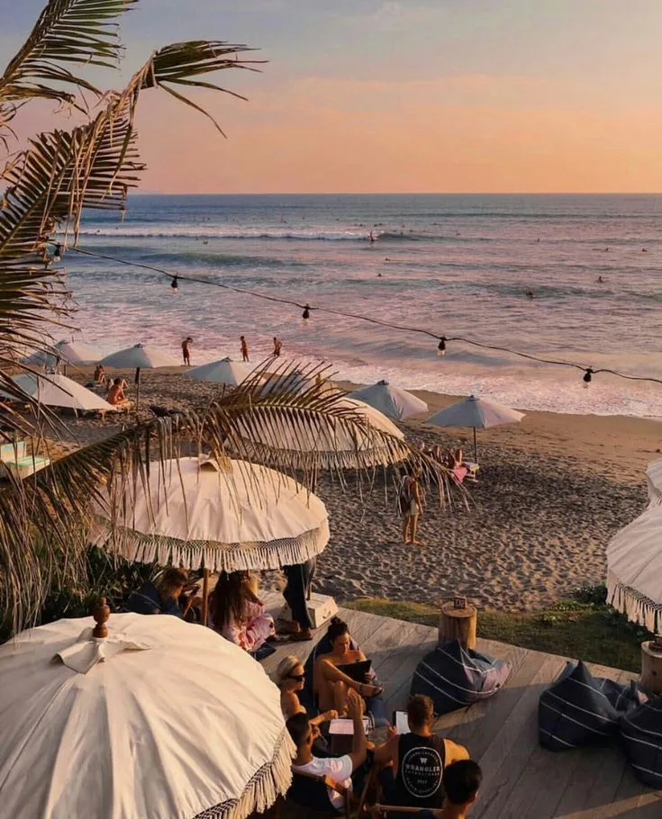 Sunset beach club in Canggu, Bali with umbrellas, string lights, and surfers in the water