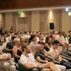 Conference attendees seated in a large hall listening to a presentation