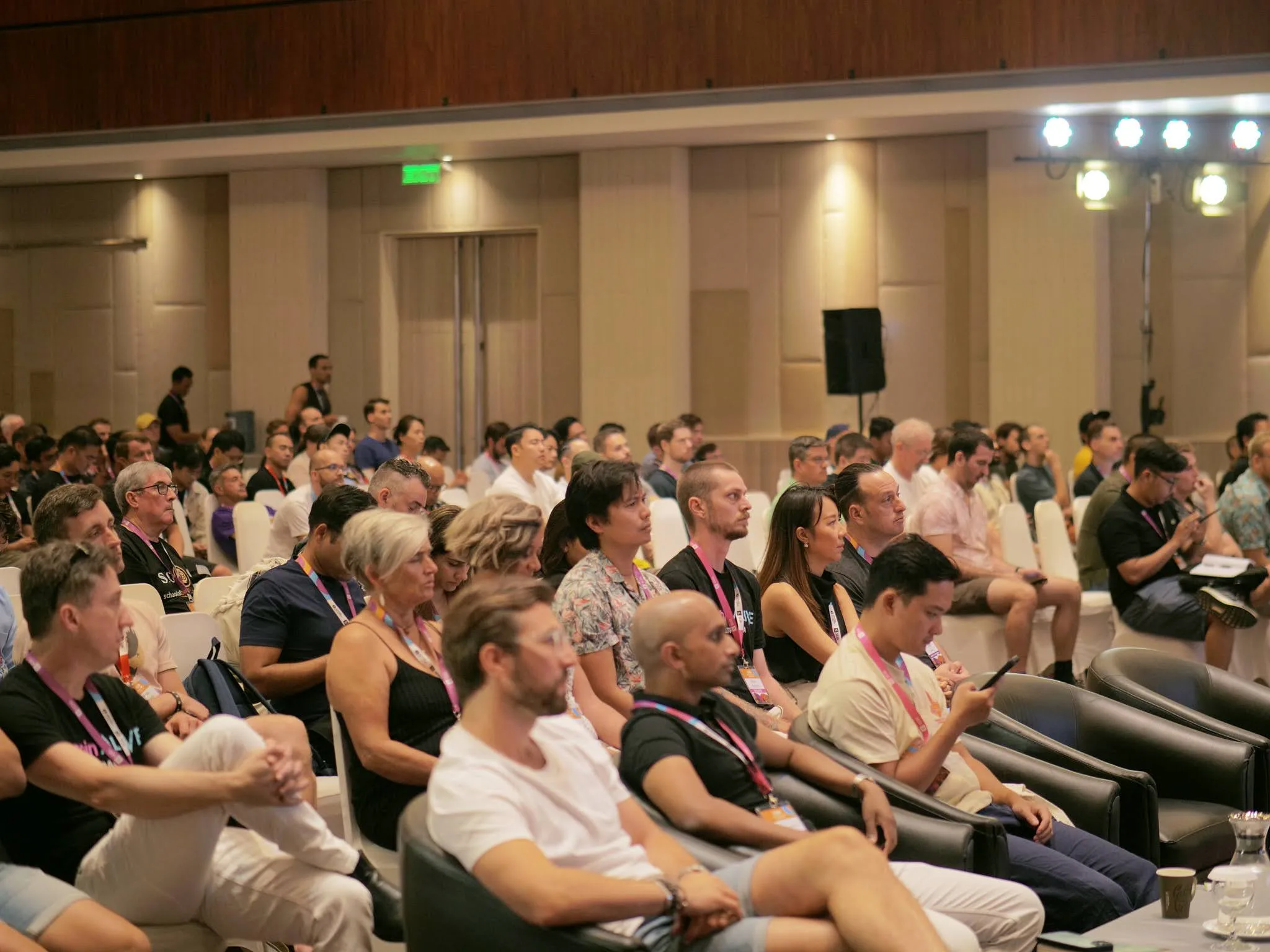Conference attendees seated in a large hall listening to a presentation
