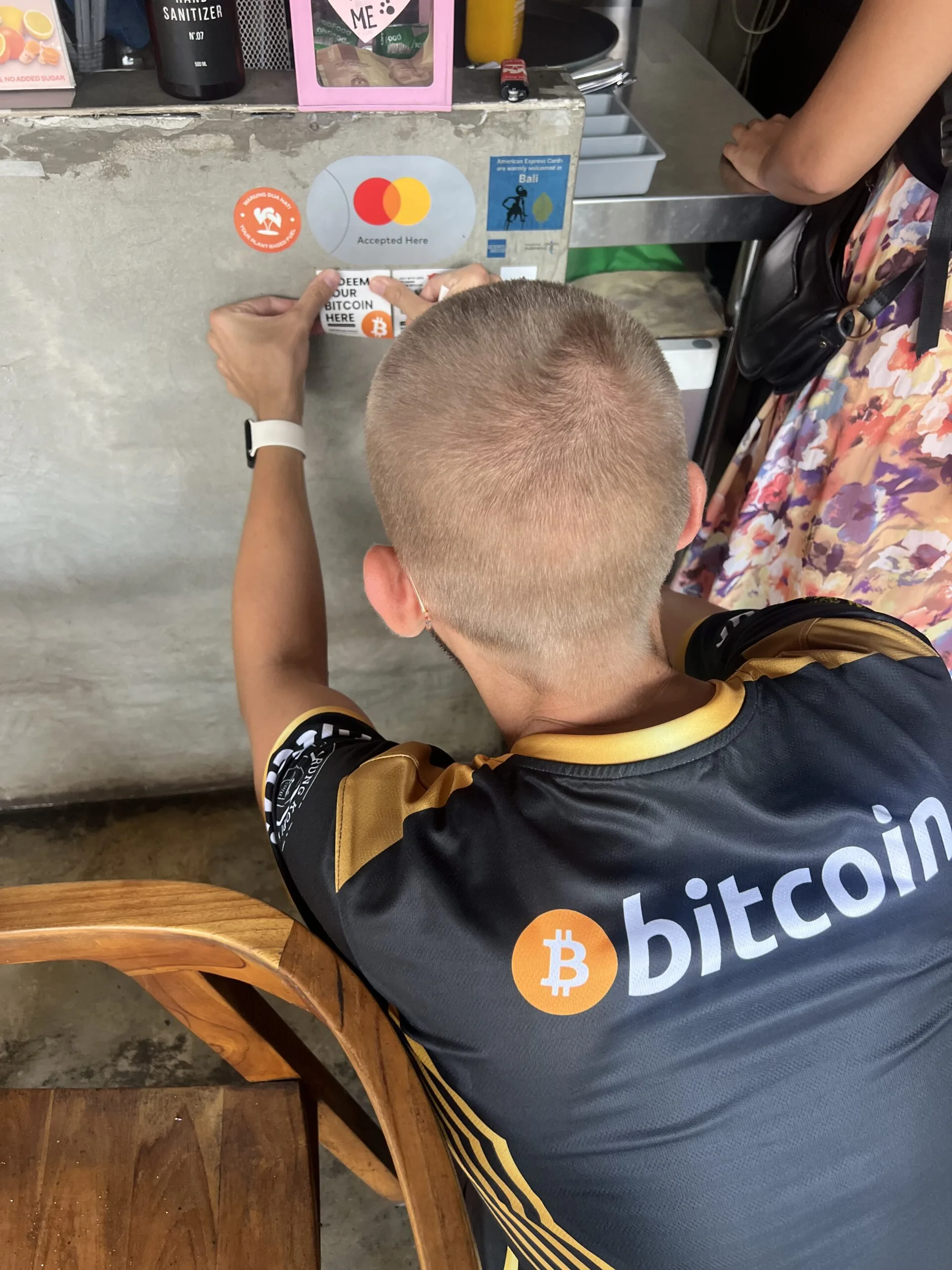 A vendor sticking a Redeem Your Bitcoin Here sign at a Bali warung that accepts Bitcoin payments