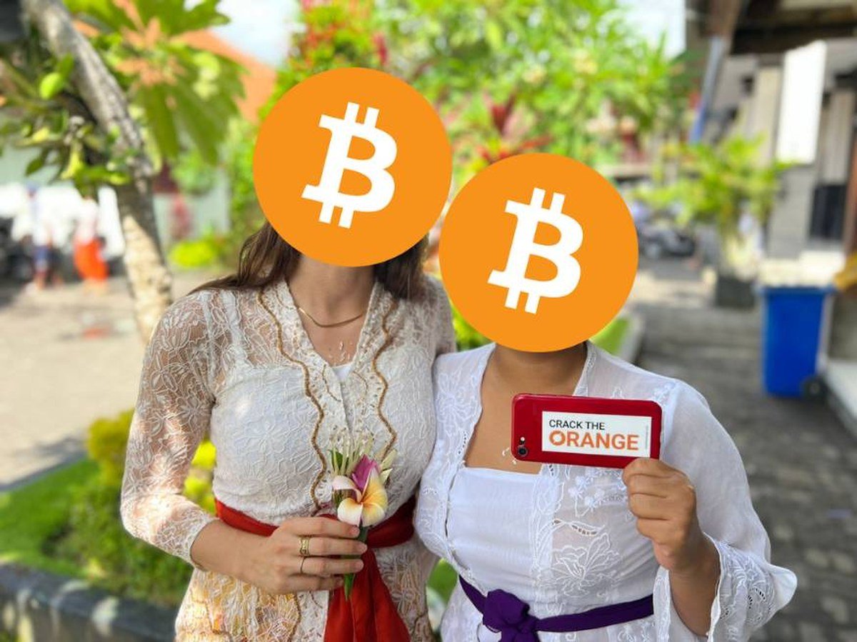 Two members of the Bitcoin Indonesia community in Bali in traditional kebaya, holding a phone, faces covered with Bitcoin logos for privacy